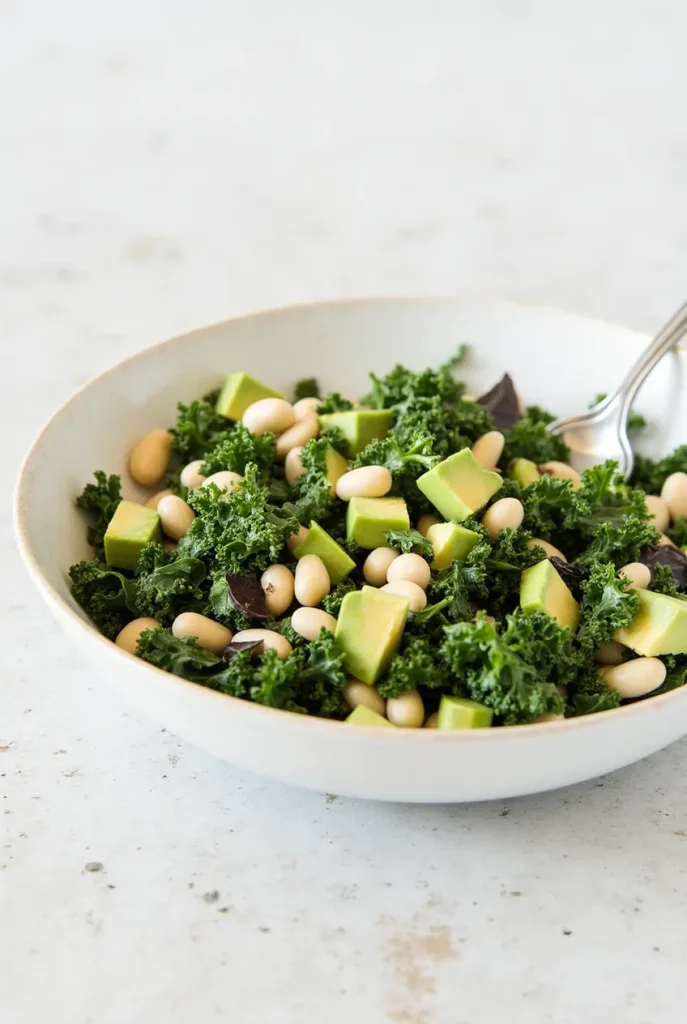 A colorful kale and white bean salad with avocado slices and a lemony dressing.