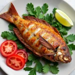 Golden air fryer tilapia fillets on a plate with lemon and parsley, next to an air fryer