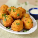 Golden-brown fried cheese bites with crispy coating and oozing melted cheese on a white plate, ready to dip.