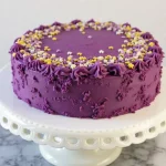 "Slice of moist Purple Velvet Cake with cream cheese frosting and edible glitter, showcasing vibrant purple layers on a marble countertop."