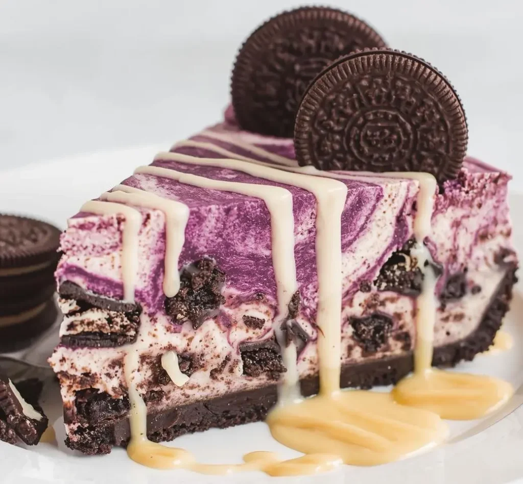 Rich and creamy Ube Oreo Cheesecake topped with crushed Oreos and purple ube swirls on a white plate.