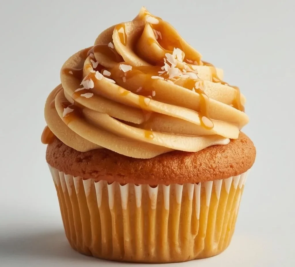 Fluffy vanilla cupcakes baked with golden caramel swirls, piled high with whipped caramel buttercream, drizzled with warm caramel sauce, and sprinkled with flaky sea salt.